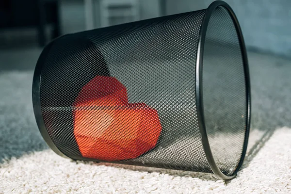 Red heart in black trash can on carpet — Stock Photo