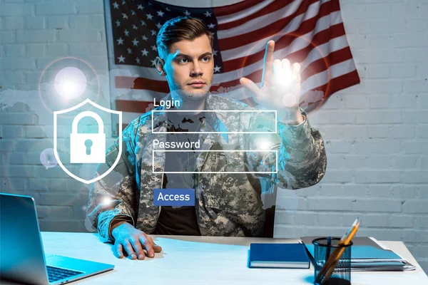 Guapo soldado en uniforme señalando con el dedo el inicio de sesión y las letras de contraseña en la oficina - foto de stock