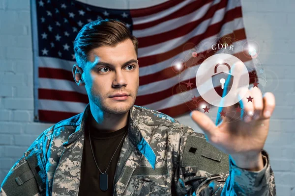 Selektiver Fokus eines gut aussehenden Soldaten, der mit dem Finger auf ein Vorhängeschloss nahe der amerikanischen Flagge zeigt — Stockfoto