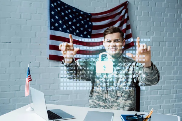 Hombre alegre en uniforme militar apuntando con los dedos al candado virtual - foto de stock