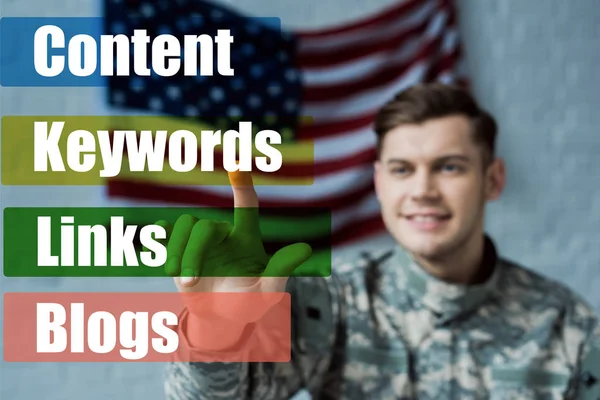 Selective focus of happy man in military uniform pointing with finger at keywords lettering — Stock Photo