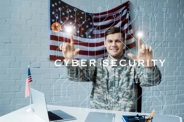 Веселый человек в военной форме, указывающий пальцами на надписи кибер-безопасности — стоковое фото