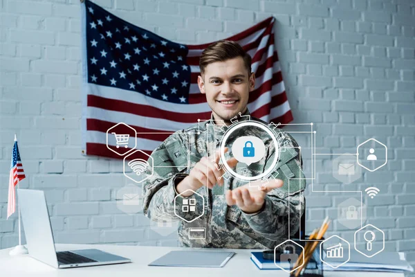 Hombre feliz en uniforme militar apuntando con el dedo al candado virtual cerca de la computadora portátil - foto de stock