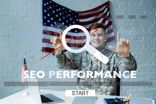 Alegre hombre en uniforme militar apuntando con los dedos a las letras de rendimiento seo - foto de stock