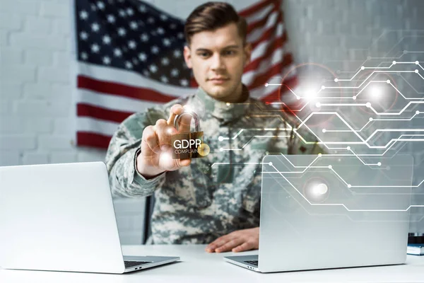 Enfoque selectivo del hombre guapo en uniforme militar con candado metálico cerca de computadoras portátiles y letras gdpr - foto de stock