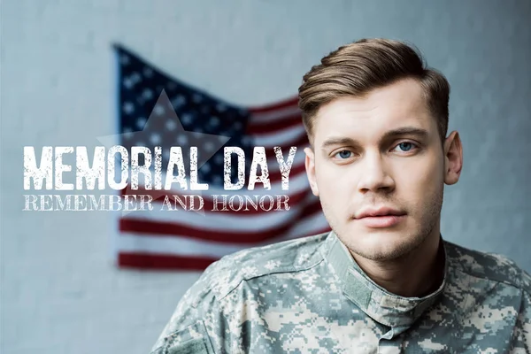 Hombre guapo en uniforme militar mirando a la cámara cerca de las letras del día memorial - foto de stock