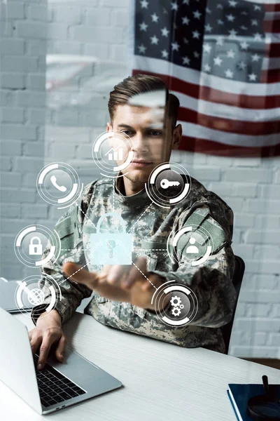 Schöner Soldat in Militäruniform, der mit dem Finger auf virtuelles Vorhängeschloss zeigt, während er Laptop benutzt — Stockfoto