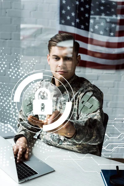 Hombre guapo en uniforme militar apuntando con el dedo al candado virtual mientras se utiliza el ordenador portátil - foto de stock