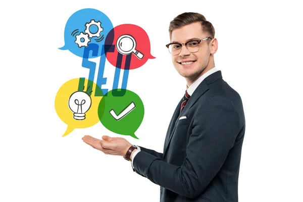 Happy businessman in glasses gesturing and smiling near seo lettering on white — Stock Photo