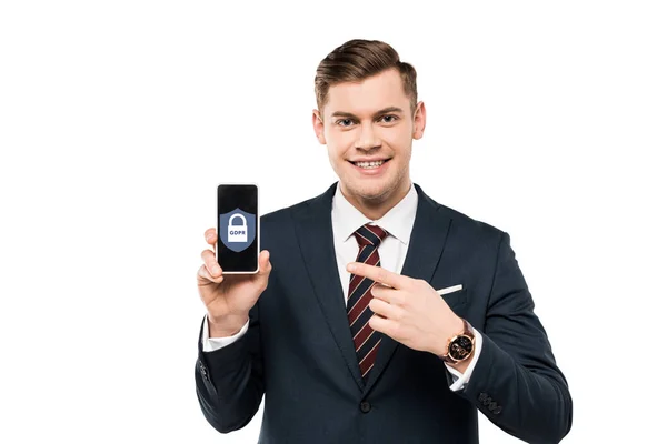 Homme d'affaires heureux en costume pointant du doigt le smartphone avec lettrage gdpr à l'écran isolé sur blanc — Photo de stock