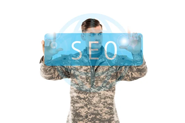 Handsome man in military uniform pointing with fingers at seo lettering on white — Stock Photo