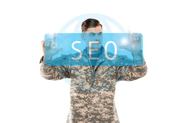 Bell'uomo in uniforme militare che punta con le dita al seo lettering sul bianco — Foto stock