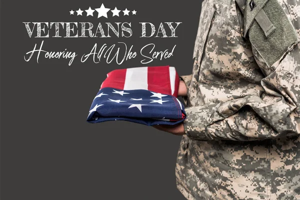 Обрізаний вид на людину у військовій формі, що тримає прапор Америки поблизу дня ветеранів, малювання на сірому — стокове фото