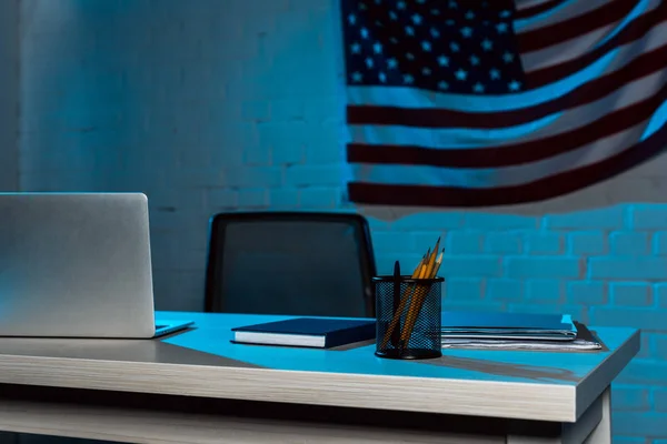 Portátil cerca de papelería en la mesa cerca de bandera americana en la oficina moderna - foto de stock