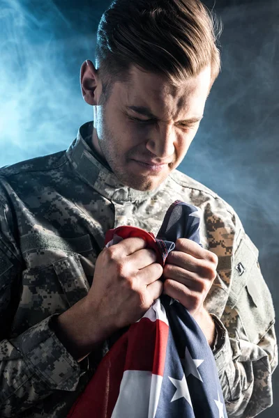 Soldado chateado segurando bandeira americana em preto com fumaça — Fotografia de Stock