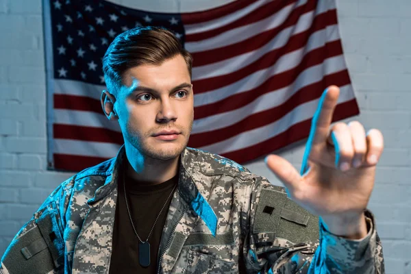 Enfoque selectivo del guapo soldado señalando con el dedo cerca de la bandera americana - foto de stock