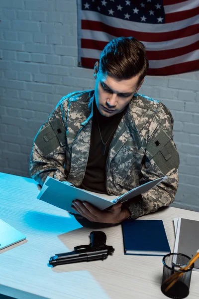 Guapo soldado sosteniendo carpeta mientras está sentado en la oficina moderna - foto de stock