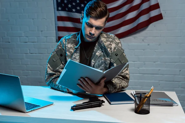 Guapo militar sosteniendo carpeta mientras está sentado en la oficina moderna - foto de stock