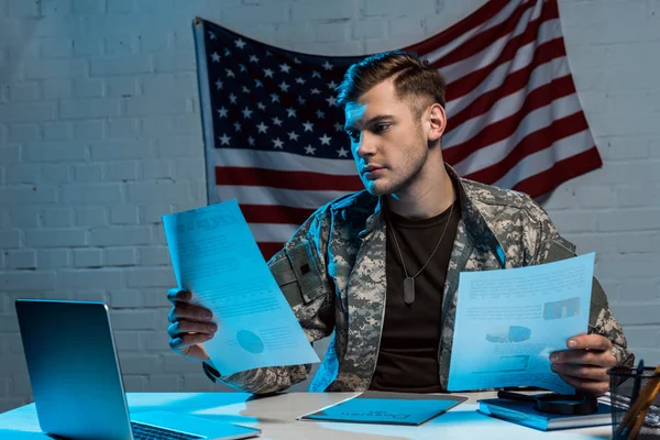 Bonito soldado segurando gráficos e gráficos enquanto sentado no escritório — Fotografia de Stock