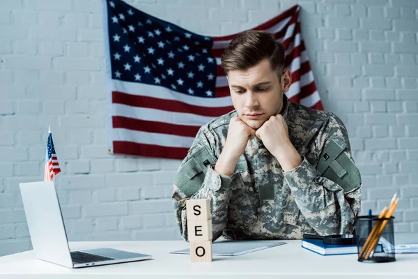 Aufgebrachter Soldat blickt im Büro auf Holzwürfel mit SEO-Schriftzug — Stockfoto