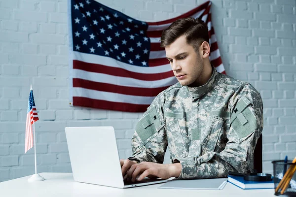 Joven soldado en uniforme usando portátil en la oficina - foto de stock