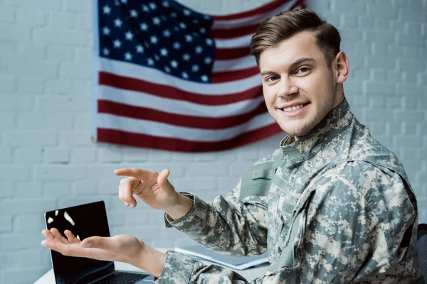 Happy military man gesturing in office near laptop with blank screen — Stock Photo