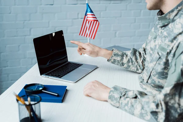 Vue recadrée de l'homme militaire pointant avec le doigt à l'ordinateur portable avec écran blanc — Photo de stock