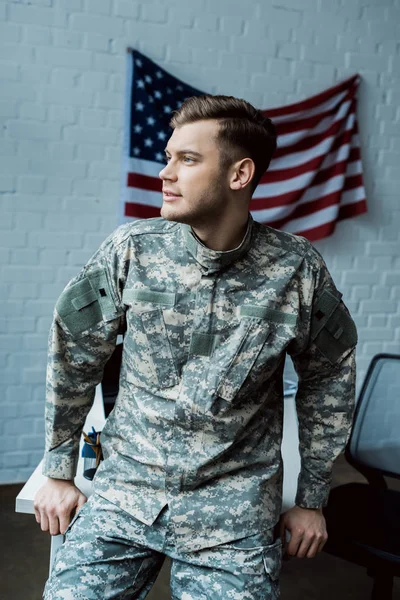 Schöner Mann in Militäruniform steht im Büro neben amerikanischer Flagge — Stockfoto