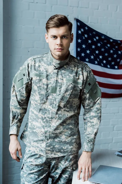 Hombre guapo en uniforme militar de pie cerca de la mesa en la oficina - foto de stock