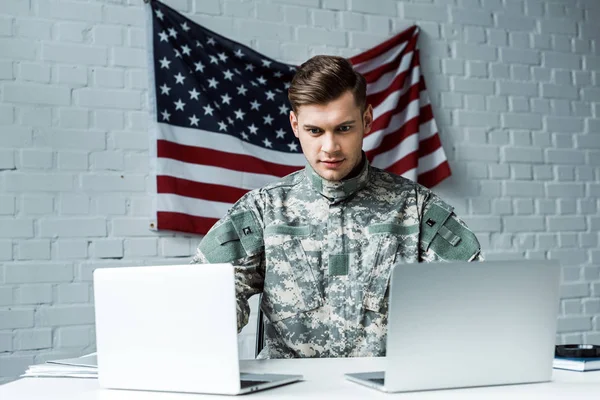 Hombre guapo en uniforme militar usando computadoras portátiles en la oficina - foto de stock