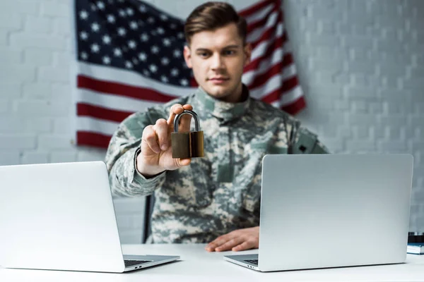 Selective focus of handsome man in military uniform holding padlock near laptops — Stock Photo