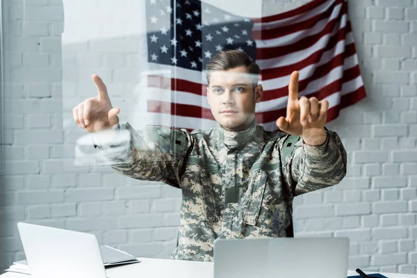 Enfoque selectivo de soldado guapo en uniforme apuntando con los dedos cerca de las computadoras portátiles en la oficina - foto de stock