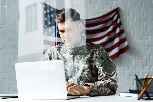 Guapo soldado en uniforme de camuflaje usando portátil en la oficina - foto de stock