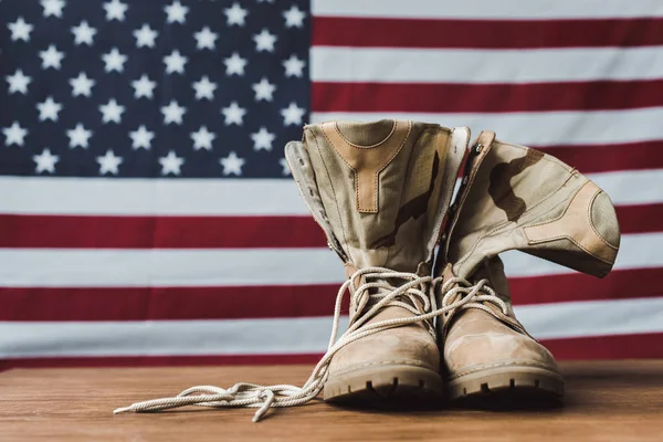Военные сапоги возле американского флага со звездами и полосками на деревянной поверхности — стоковое фото