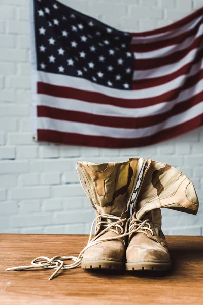 Botas militares perto da bandeira americana com estrelas e listras na parede de tijolos — Fotografia de Stock