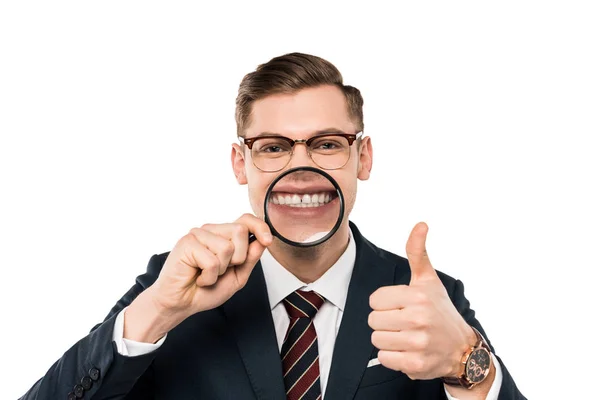 Alegre hombre de negocios en gafas mostrando el pulgar hacia arriba y sosteniendo lupa mientras sonríe aislado en blanco - foto de stock