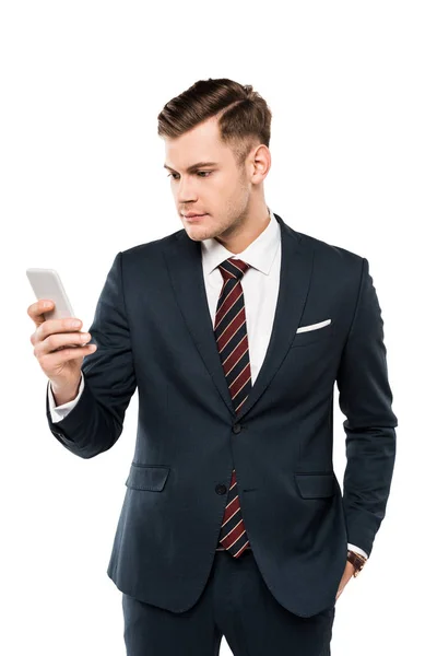 Hombre de negocios guapo en traje mirando teléfono inteligente aislado en blanco - foto de stock