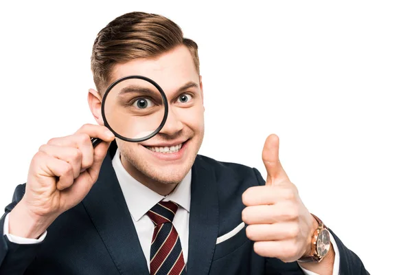 Alegre hombre de negocios mostrando el pulgar hacia arriba y la celebración de lupa cerca de ojo aislado en blanco - foto de stock