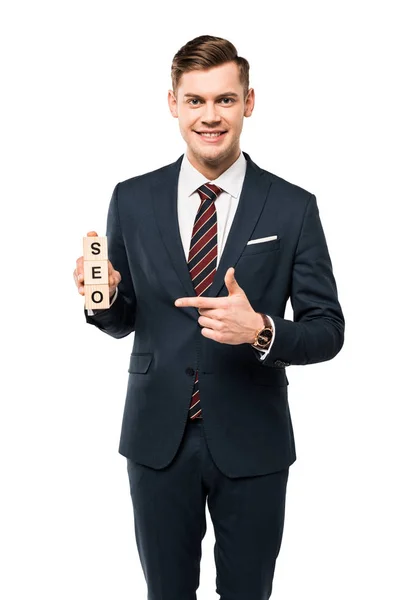 Vista ritagliata di felice uomo d'affari che punta con il dito a cubi di legno con seo lettering isolato su bianco — Foto stock