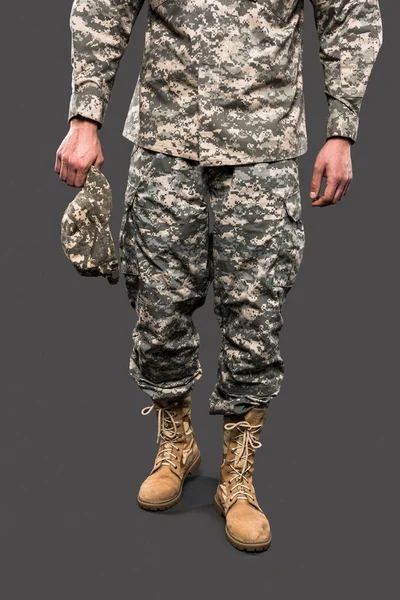 Обрізаний вид солдата тримає шапку і стоїть ізольовано на сірому — стокове фото