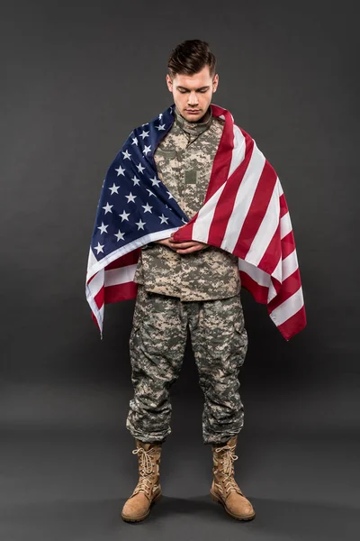 Hombre molesto en uniforme militar con bandera americana de pie sobre gris - foto de stock