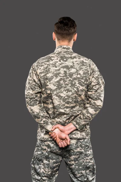 Vista trasera del soldado de pie con las manos apretadas aisladas en gris - foto de stock