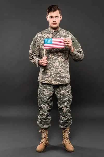 Homem sério em uniforme militar segurando bandeira americana em cinza — Fotografia de Stock