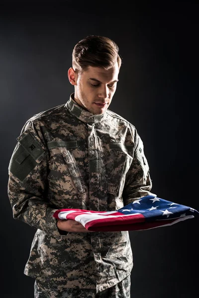 Homem de uniforme militar olhando para a bandeira americana em preto — Fotografia de Stock