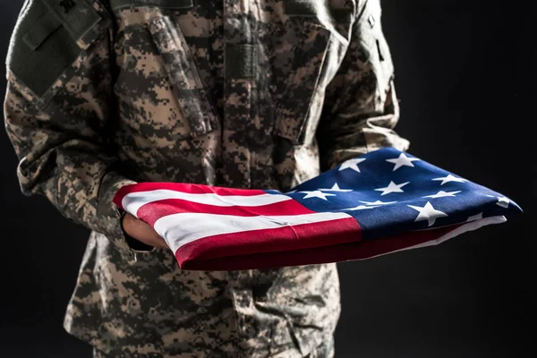 Cropped view of man in military uniform holding flag of america isolated on black — Stock Photo