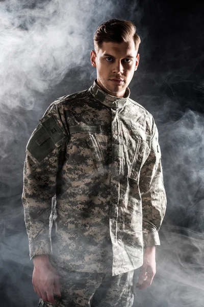 Hombre guapo en uniforme militar mirando a la cámara en negro con humo - foto de stock