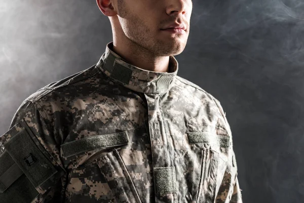 Cropped view of serious soldier in military uniform on black with smoke — Stock Photo