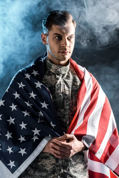 Soldado en uniforme militar con las manos apretadas y bandera americana en negro con humo - foto de stock