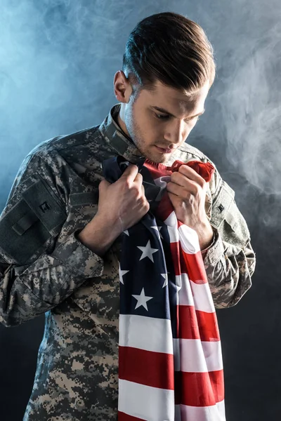 Upset soldier holding american flag on black with smoke — Stock Photo