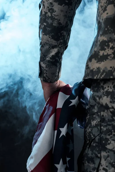 Vista ritagliata di soldato che tiene bandiera americana su nero con fumo — Foto stock
